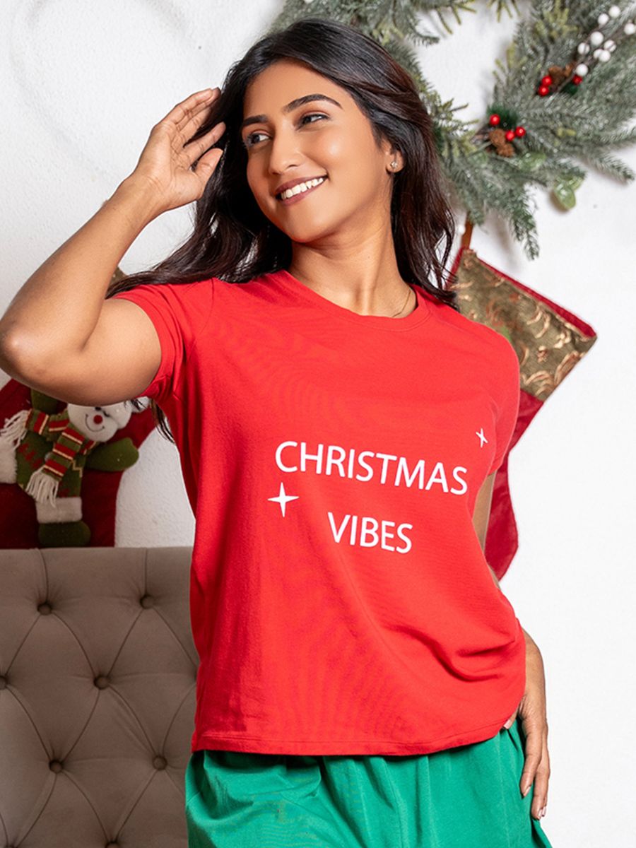 Woman wearing a red 'Christmas Vibes' t-shirt with festive decorations in the background.