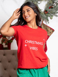 Woman wearing a red 'Christmas Vibes' t-shirt with festive decorations in the background.