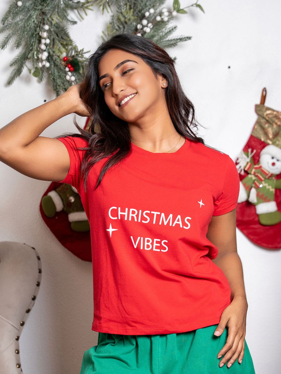 Woman wearing a red 'Christmas Vibes' shirt in a festive setting with stockings and decorations.