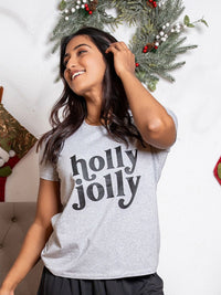 Woman wearing a 'holly jolly' shirt in front of a Christmas wreath.