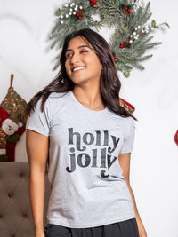 Woman wearing a 'holly jolly' shirt in front of a Christmas wreath.