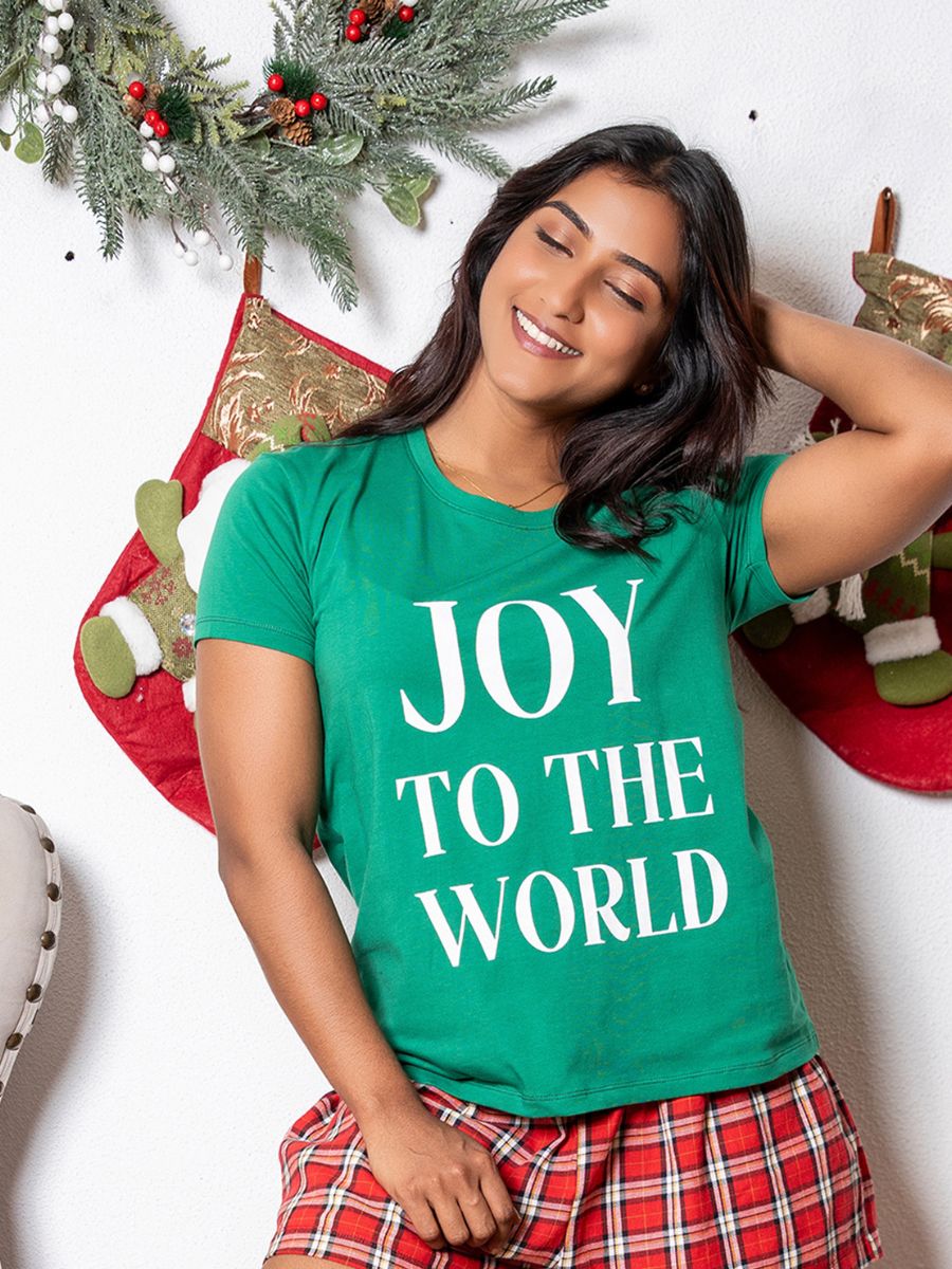 Person wearing a green 'JOY TO THE WORLD' t-shirt with Christmas decorations in the background.