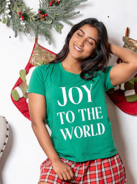 Person wearing a green 'JOY TO THE WORLD' t-shirt with Christmas decorations in the background.