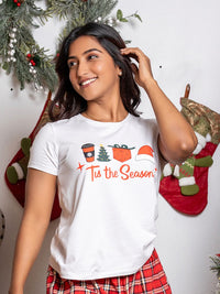Woman wearing a 'Tis the Season' t-shirt with Christmas graphics against a festive background.