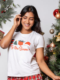 Woman wearing a white t-shirt with Christmas-themed design in front of a decorated Christmas tree.