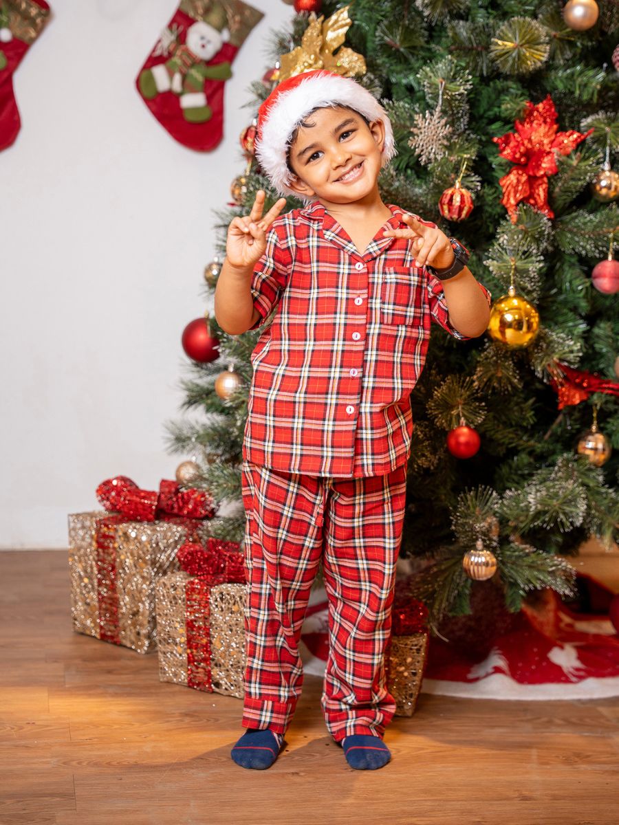 Child in red plaid pajamas standing in front of a decorated Christmas tree with presents.