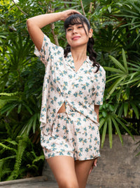 Woman wearing a floral pajama set standing in front of green foliage