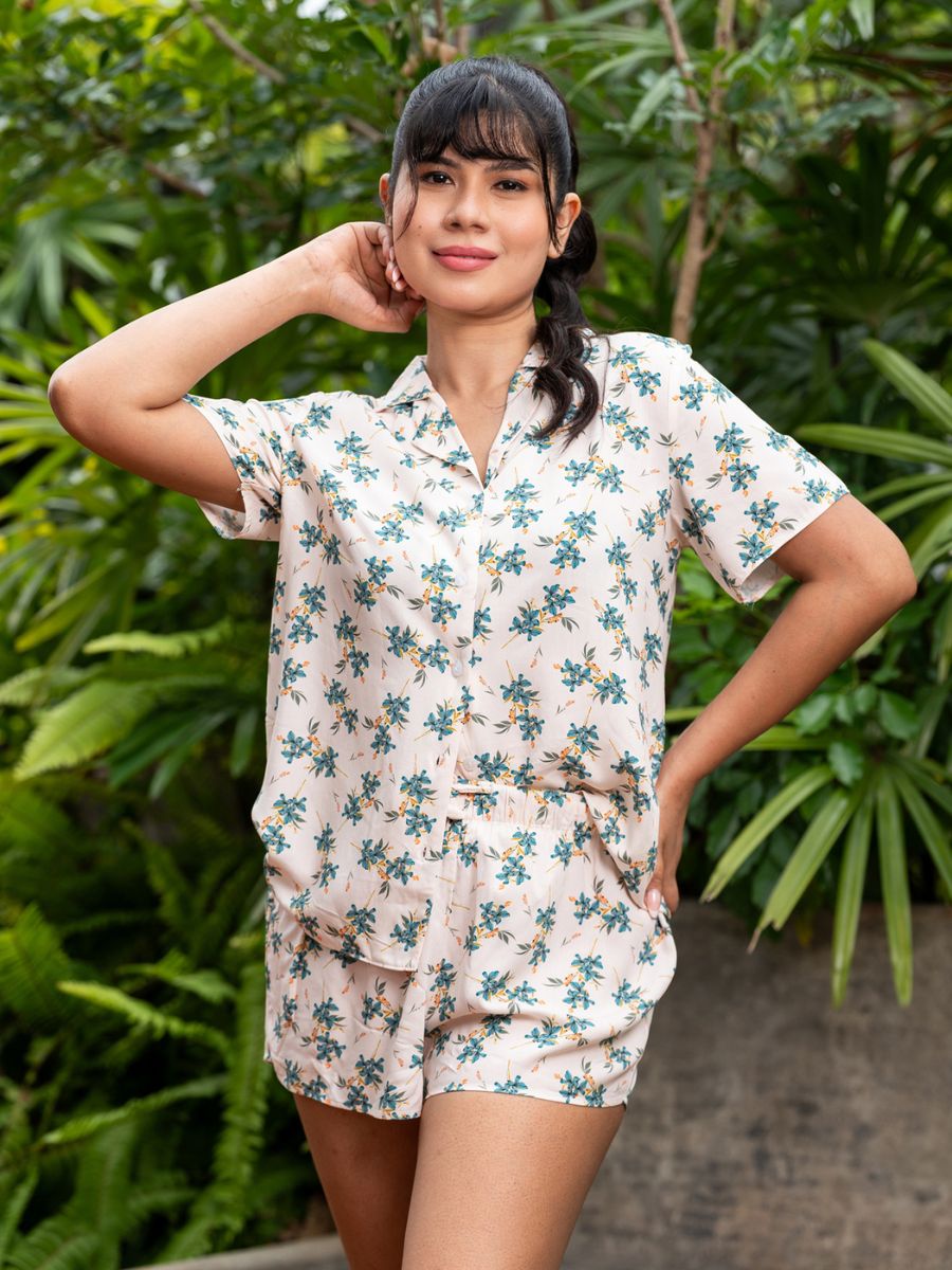 Woman wearing a floral pajama set standing in front of green foliage