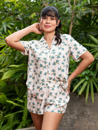 Woman wearing a floral pajama set standing in front of green foliage