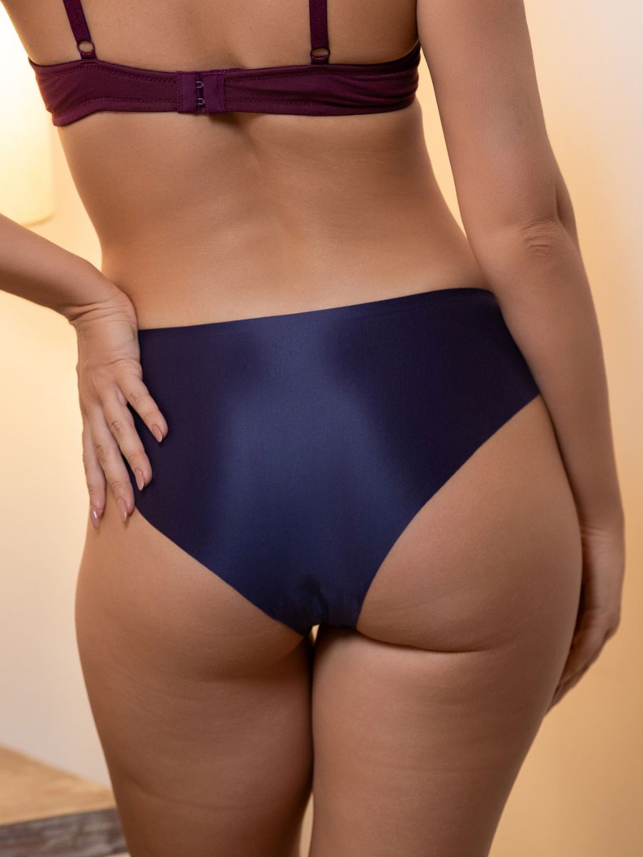 Person wearing a dark purple bra and underwear set against a neutral background